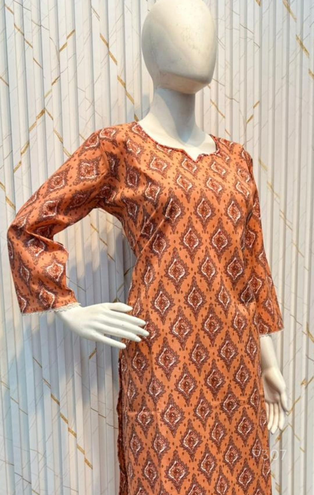 Mannequin wearing an orange patterned dress against a decorative wall.