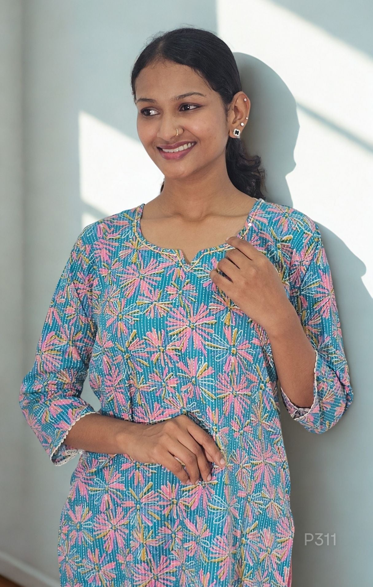 Woman wearing a colorful floral dress against a white wall