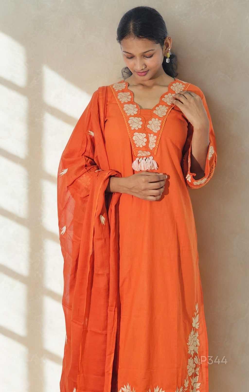 Woman wearing an orange traditional outfit with floral patterns indoors.