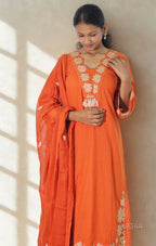 Woman wearing an orange traditional outfit with floral patterns indoors.