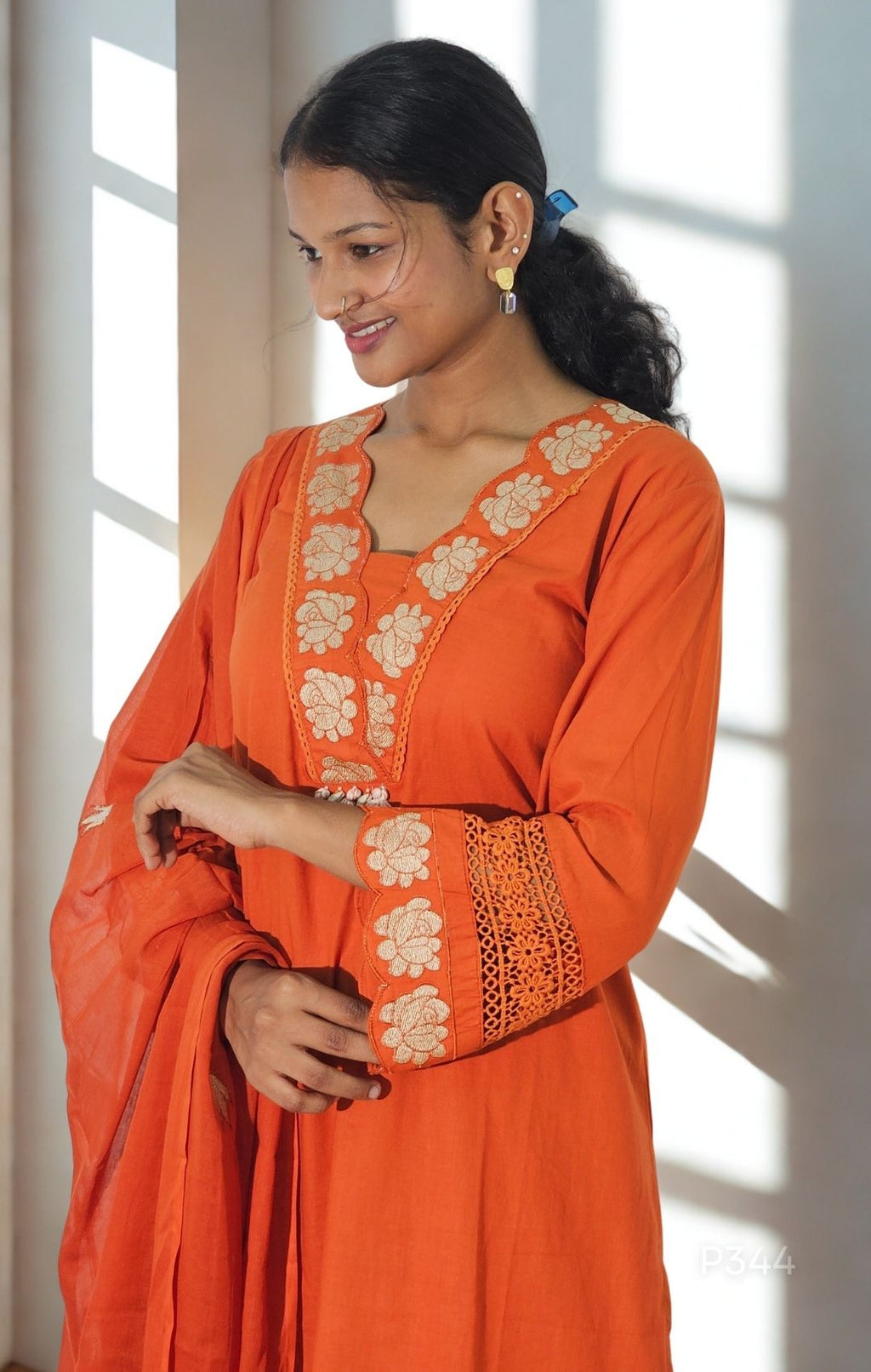 Woman wearing an orange traditional outfit with floral patterns indoors.