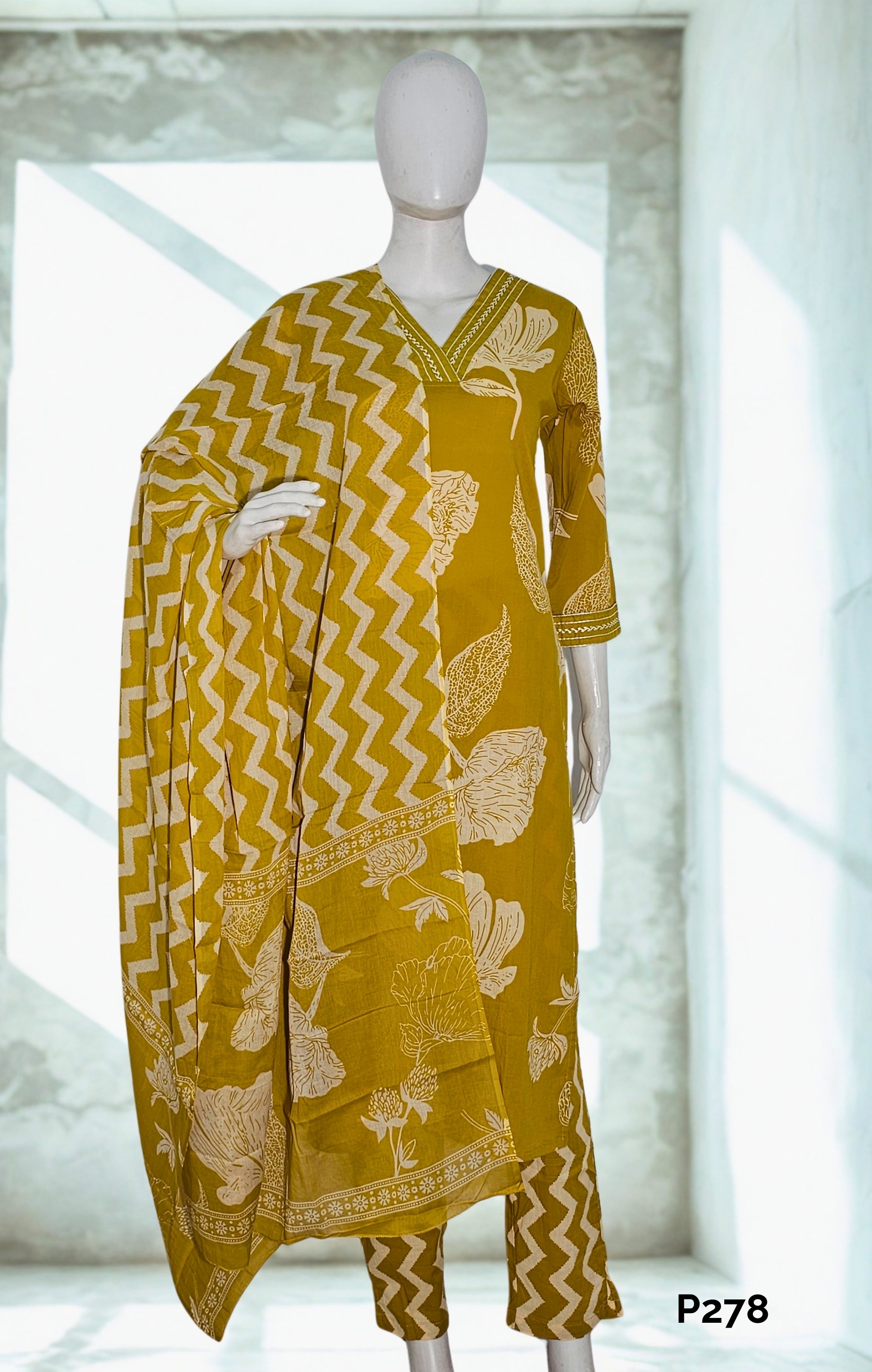 Mannequin wearing a mustard yellow kurta with white floral patterns and matching dupatta in a bright room.