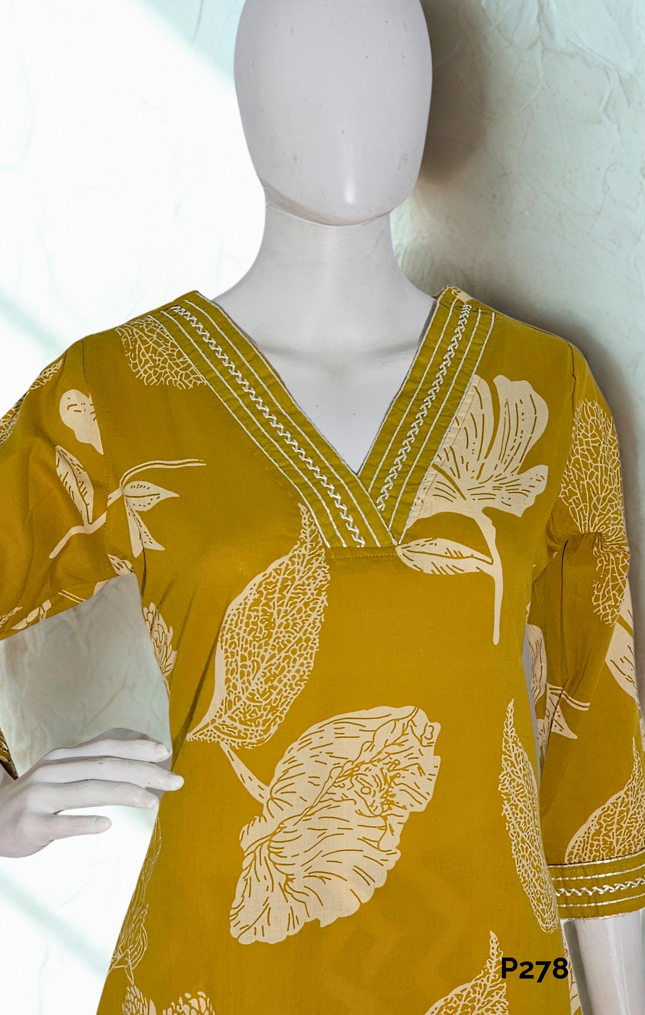 Yellow top with floral patterns on a mannequin against a white background
