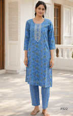 Woman wearing a blue traditional outfit with floral patterns on a white porch.