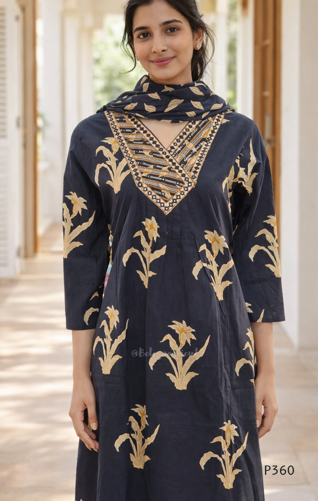 Woman wearing a black dress with gold floral patterns and embellishments.