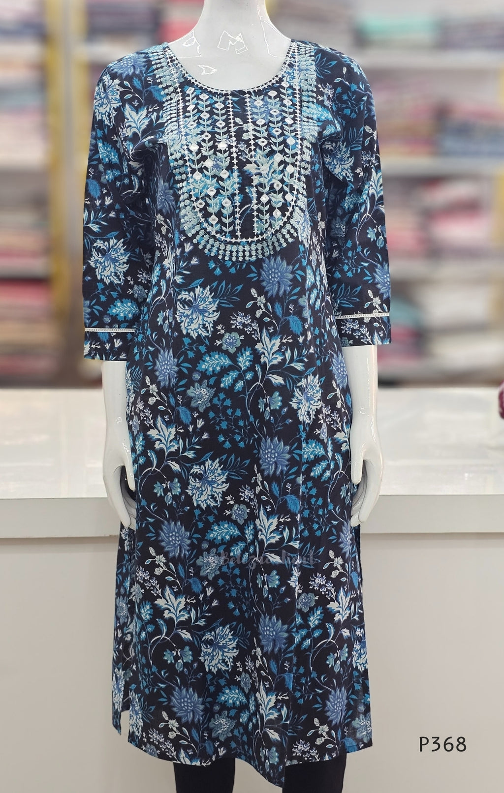 Blue floral dress on a mannequin with a blurred bookshelf background