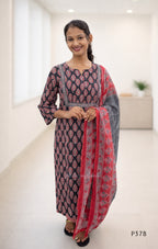 Woman wearing a traditional outfit with a black and red patterned dress and dupatta in a white room.