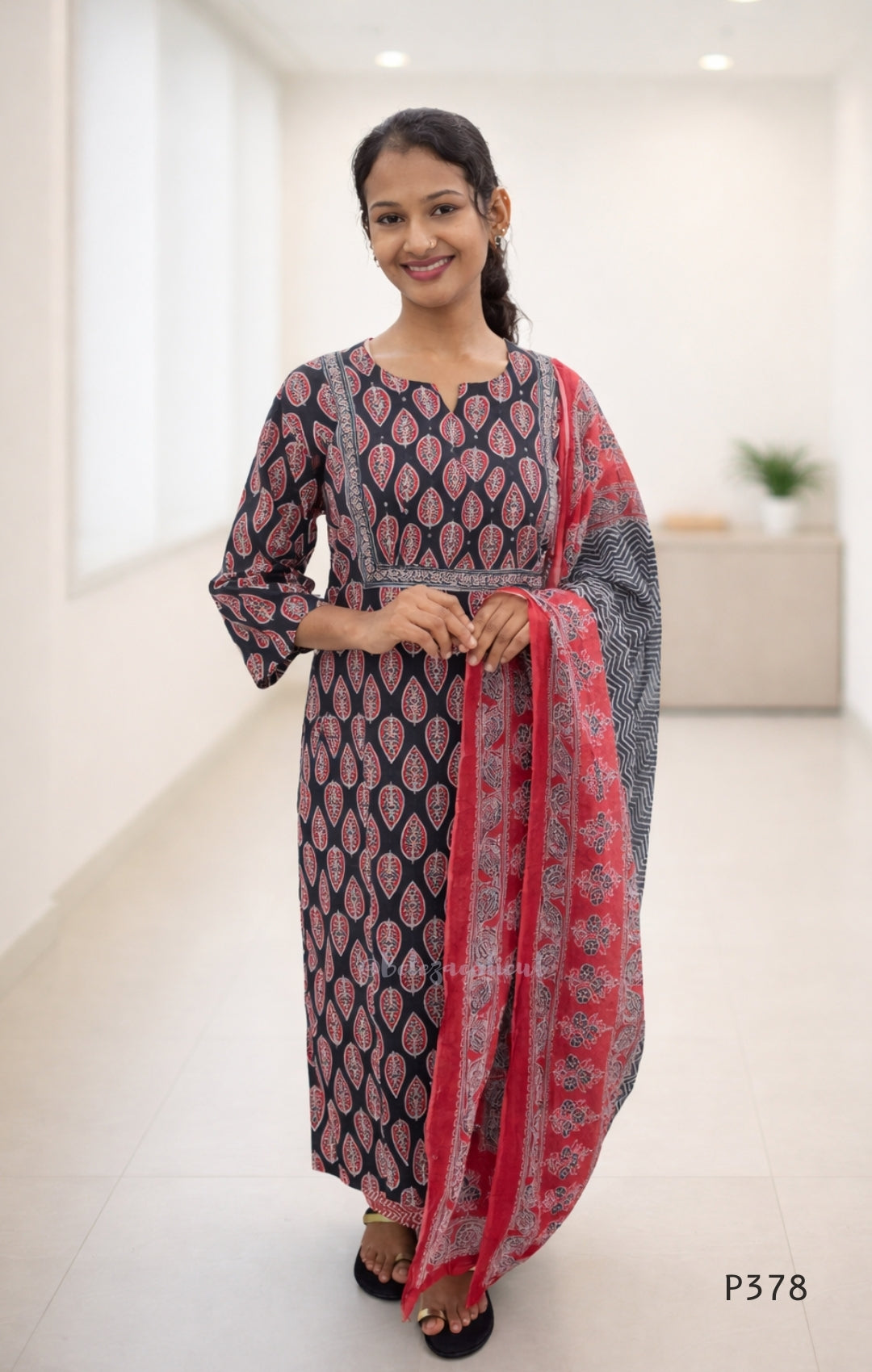 Woman wearing a traditional outfit with a black and red patterned dress and dupatta in a white room.