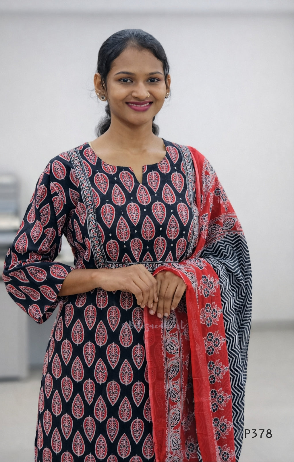 Woman wearing a black and red patterned kurta with a red dupatta against a white background