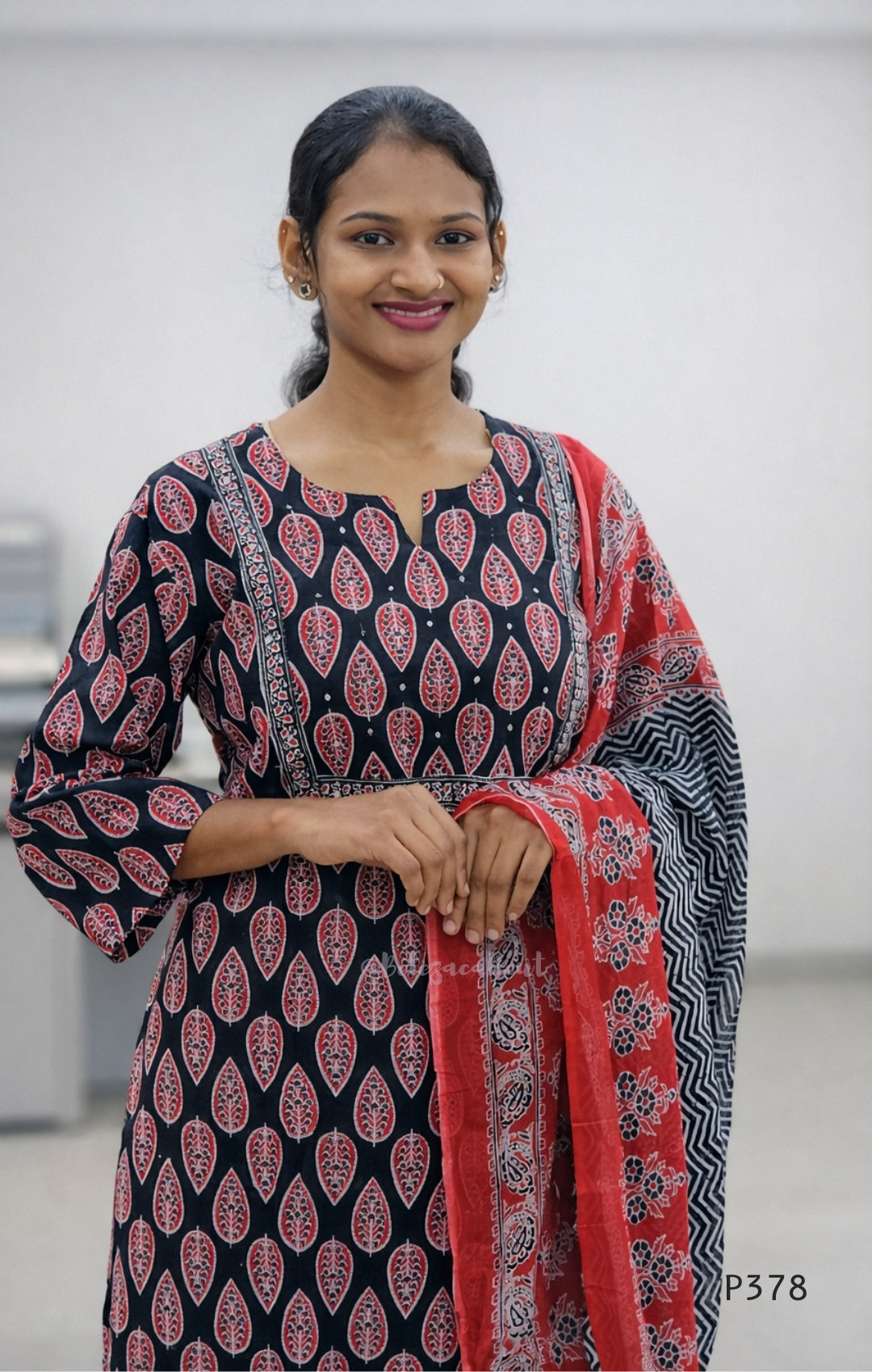 Woman wearing a black and red patterned kurta with a red dupatta against a white background