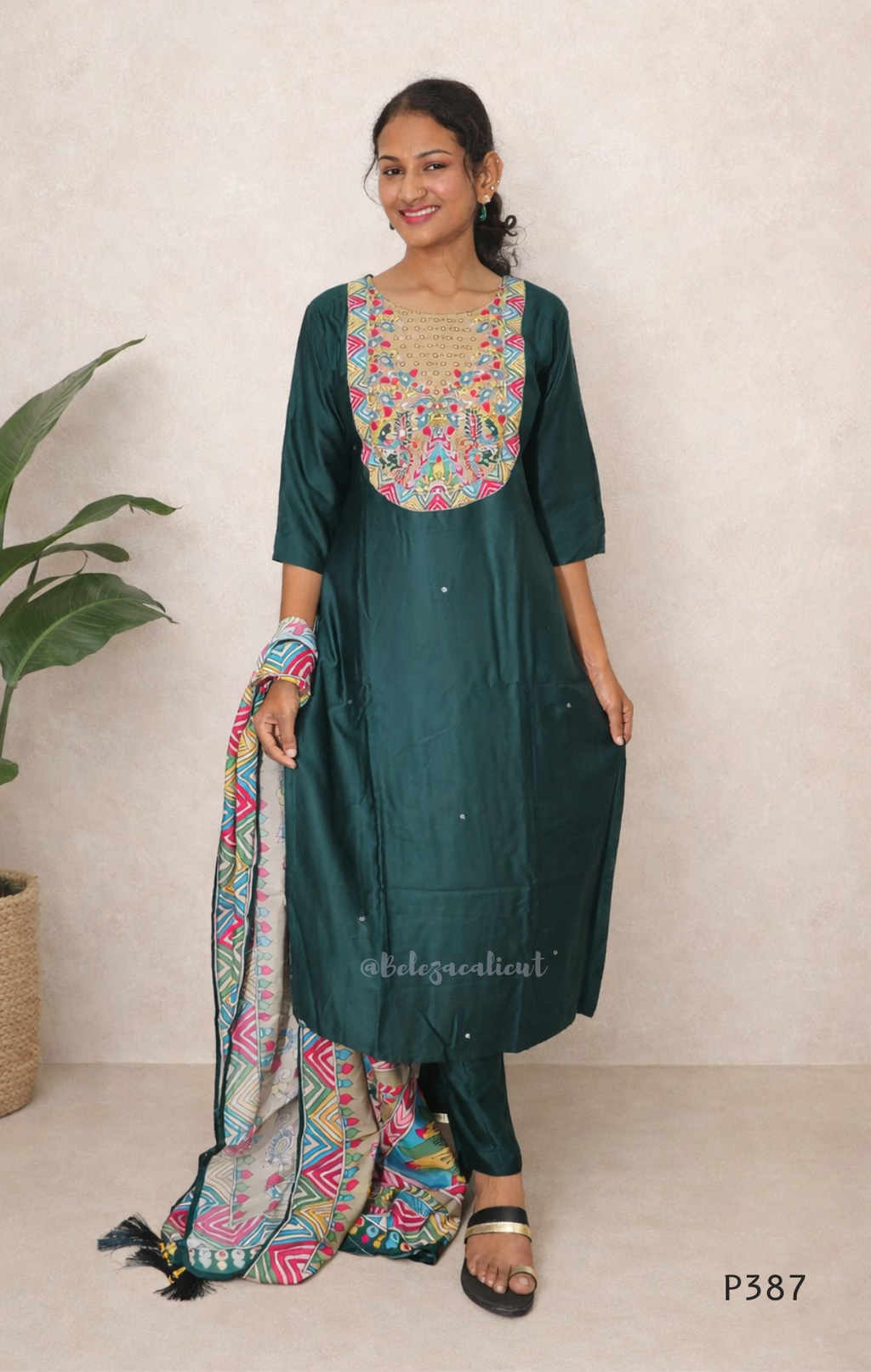 Woman wearing a green traditional outfit with colorful embroidery against a beige background