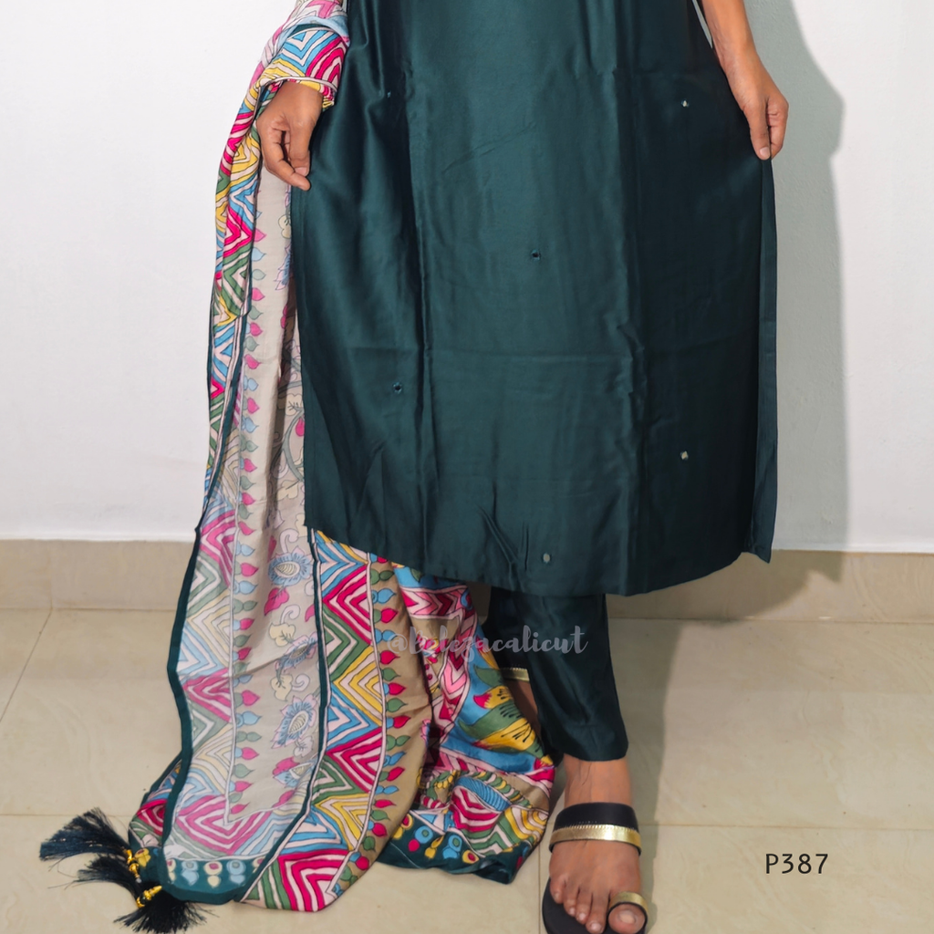 Person wearing a dark green outfit with colorful fabric draped over one shoulder on a plain background