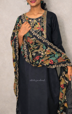 Woman wearing a black outfit with a floral embroidered dupatta against a plain background