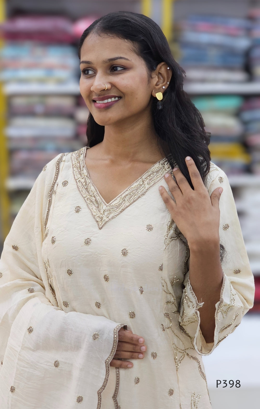 Woman wearing a cream-colored traditional outfit with intricate designs, standing outdoors.
