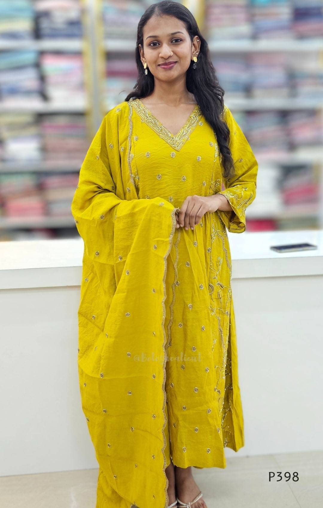 Woman wearing a yellow traditional outfit with intricate designs, standing indoors.