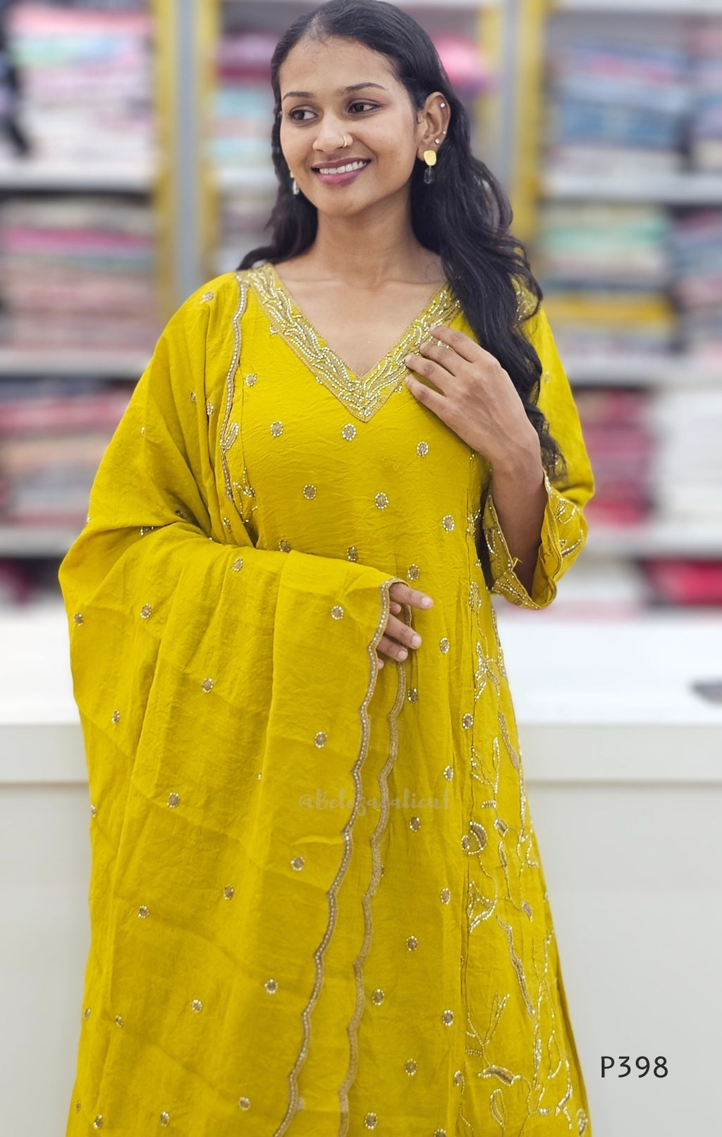 Woman wearing a yellow traditional outfit with intricate designs, standing against a blurred background.