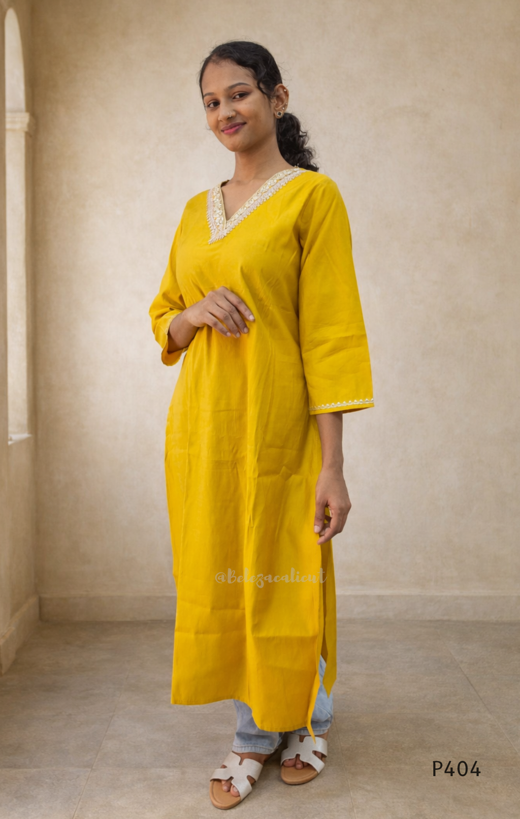 Woman wearing a yellow kurta with white trim against a beige wall.