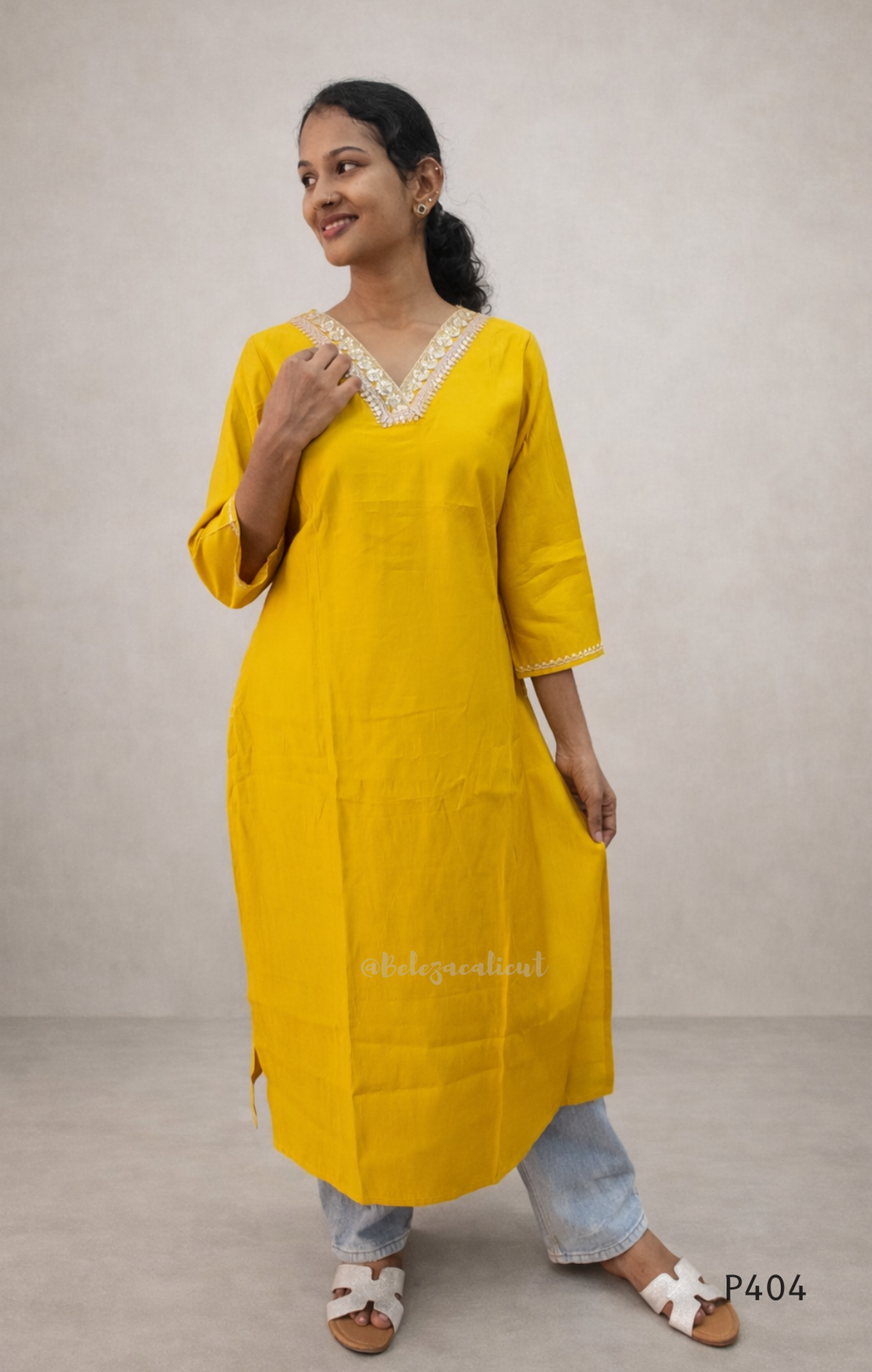 Woman wearing a yellow kurta with white lace details on a plain background