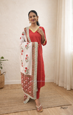 Woman wearing a red traditional outfit with a white dupatta featuring red floral patterns, standing indoors.