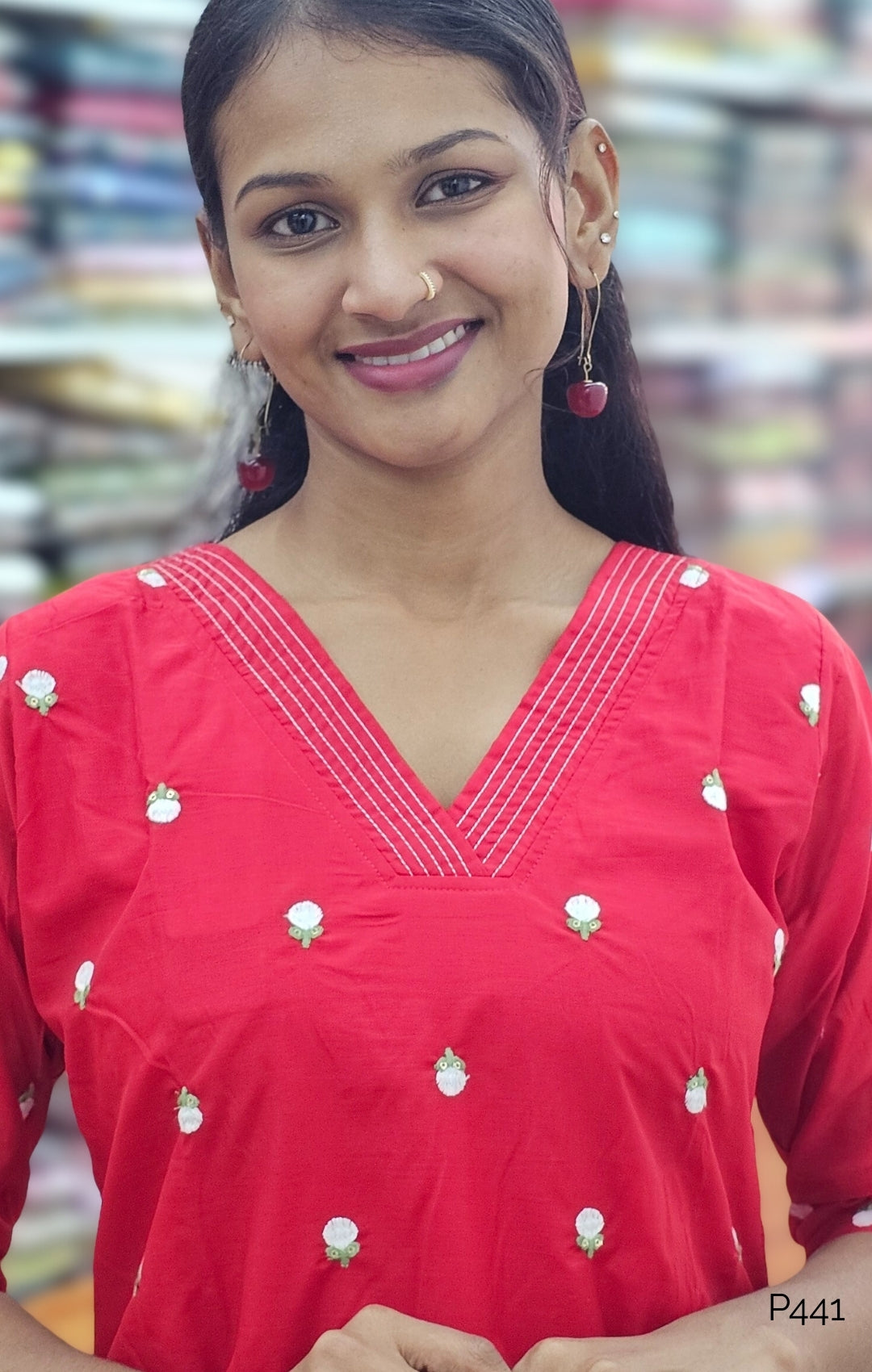 Woman wearing a red traditional outfit with white patterns in a blurred indoor setting