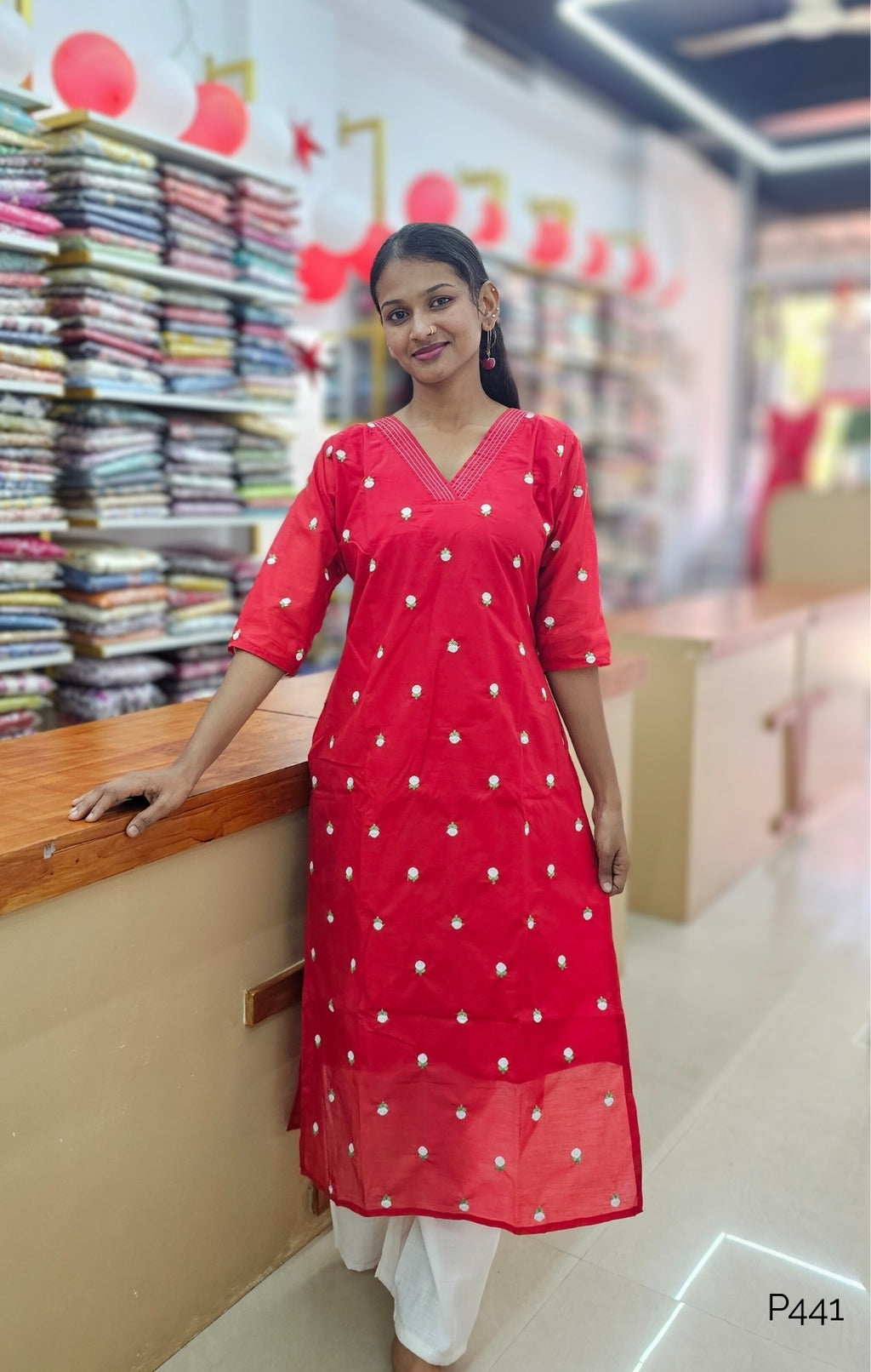 Woman in a red dress standing in a store with fabric on shelves.
