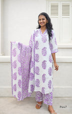 Woman wearing a white outfit with purple floral patterns in front of a white wall.