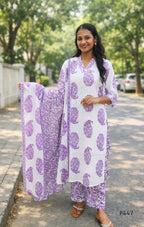 Woman wearing a white outfit with purple floral patterns on a street.