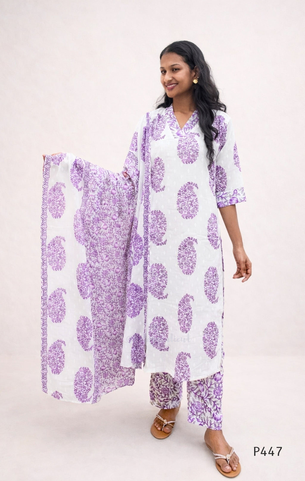 Woman wearing a white outfit with purple floral patterns on a plain background