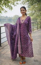 Woman in a purple traditional outfit standing outdoors by a body of water.