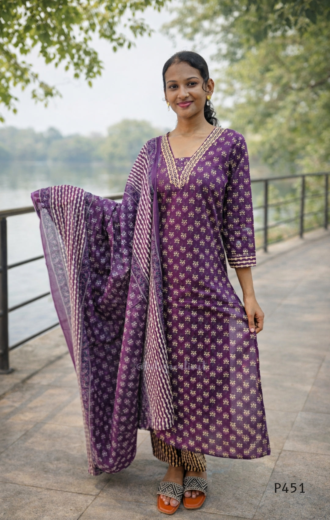Woman in a purple traditional outfit standing outdoors by a body of water.