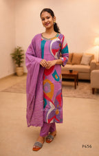 Woman wearing a colorful traditional outfit with a purple dupatta in a living room setting.