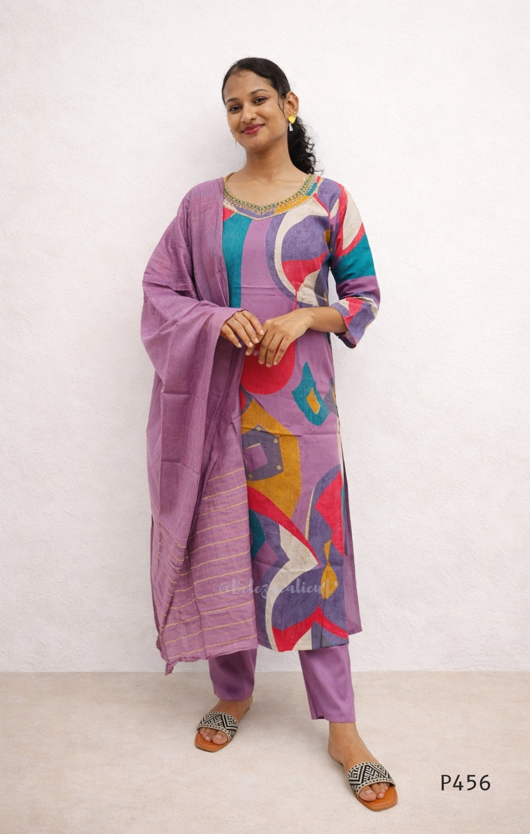 Woman wearing a colorful outfit with a purple dupatta against a white background