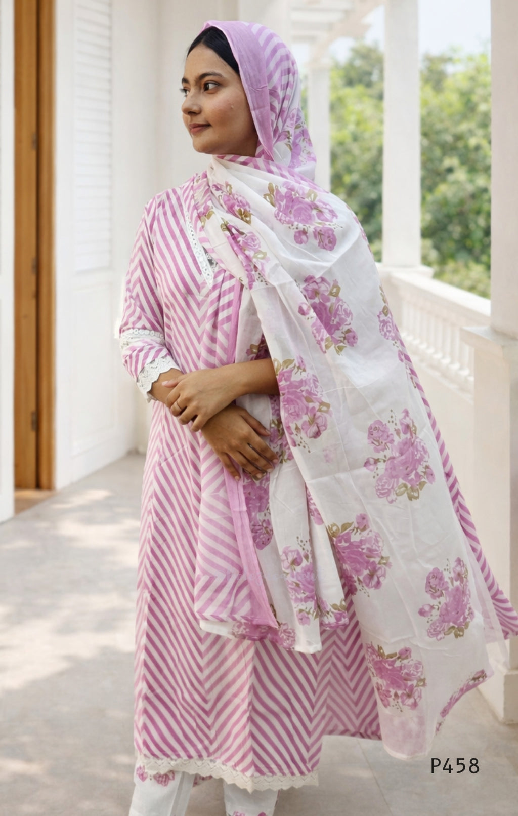 Woman wearing a pink and white traditional outfit with a floral dupatta, standing on a wooden deck.