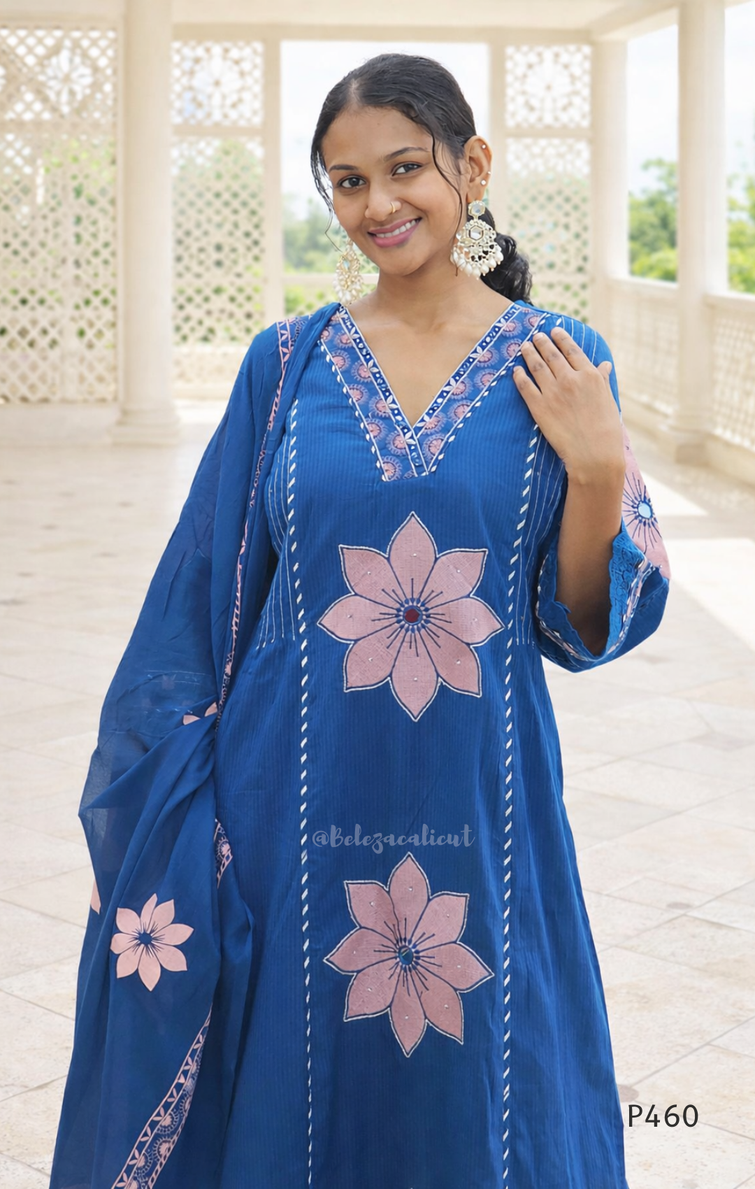 Woman wearing a blue embroidered dress with pink flowers in an outdoor setting.