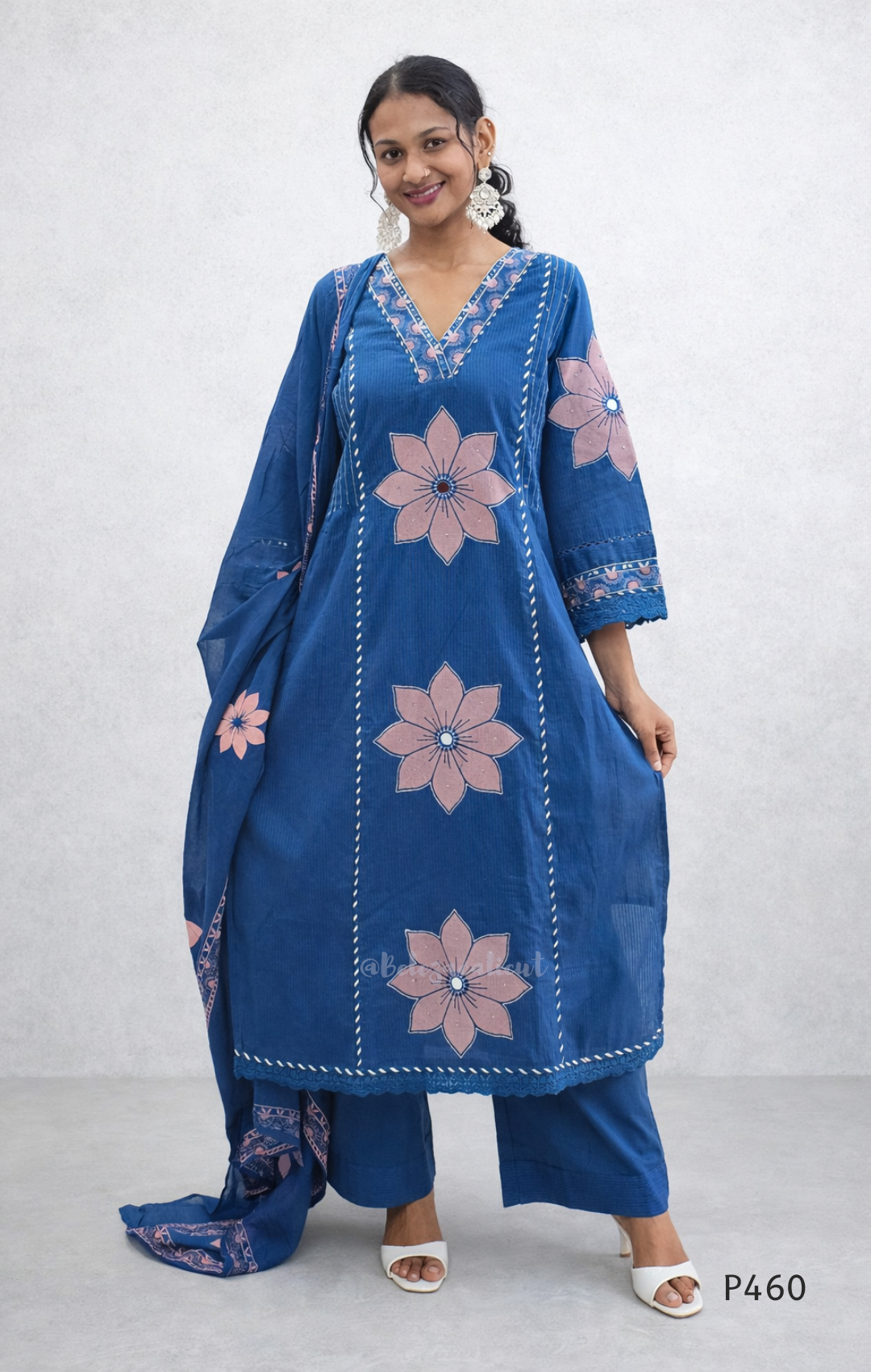 Woman wearing a blue embroidered outfit with pink flowers on a white background