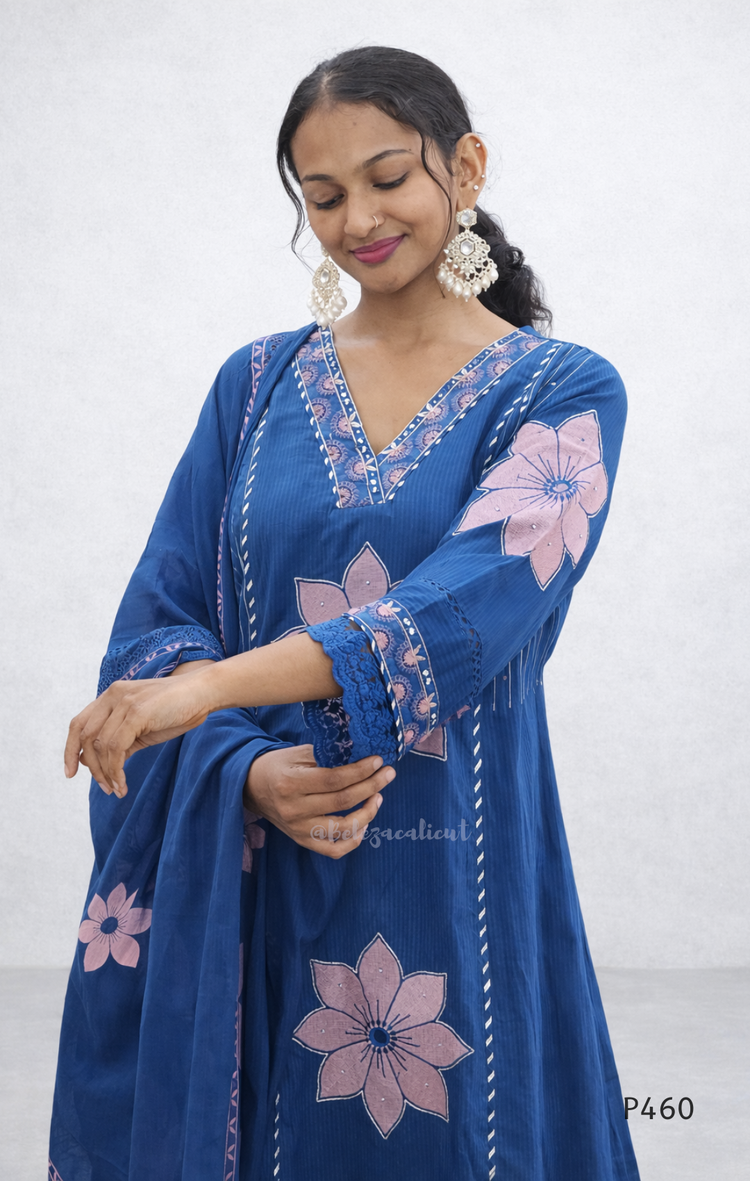 Woman wearing a blue embroidered dress with pink flowers on a white background