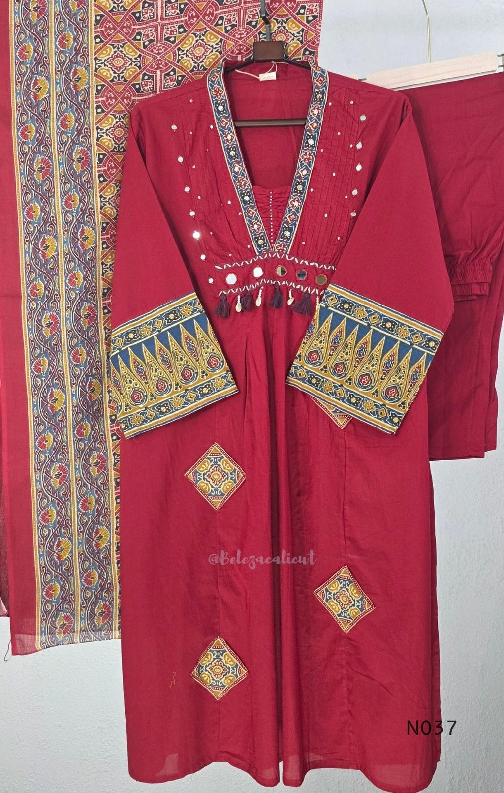 Raspberry red cotton 3-piece churidar set with a printed V-neck border, mirror-and-tassel yoke, diamond motifs, printed sleeves, straight pants and a printed dupatta.