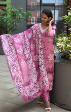 Woman wearing a pink traditional outfit with white patterns outdoors.
