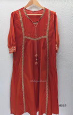 Rust-orange cotton churidar set with decorative patchwork-style trims, gathered yoke, straight pants and printed dupatta.