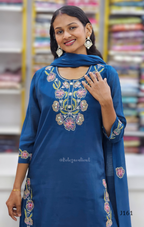 Woman wearing a blue embroidered outfit with a matching scarf in a store setting.
