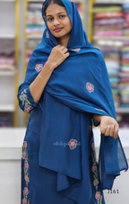 Woman wearing a blue embroidered scarf with a blurred bookshelf background