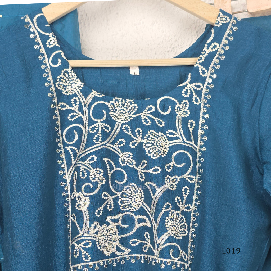 Deep teal blue silk blend 3-piece churidar set with square white floral threadwork embroidery yoke with bead droplet border, straight cut kurti with 3/4 sleeves, matching plain teal bottom with drawstring, and teal chiffon dupatta with scattered silver sequin dots, Indian ethnic wear from Beleza Calicut